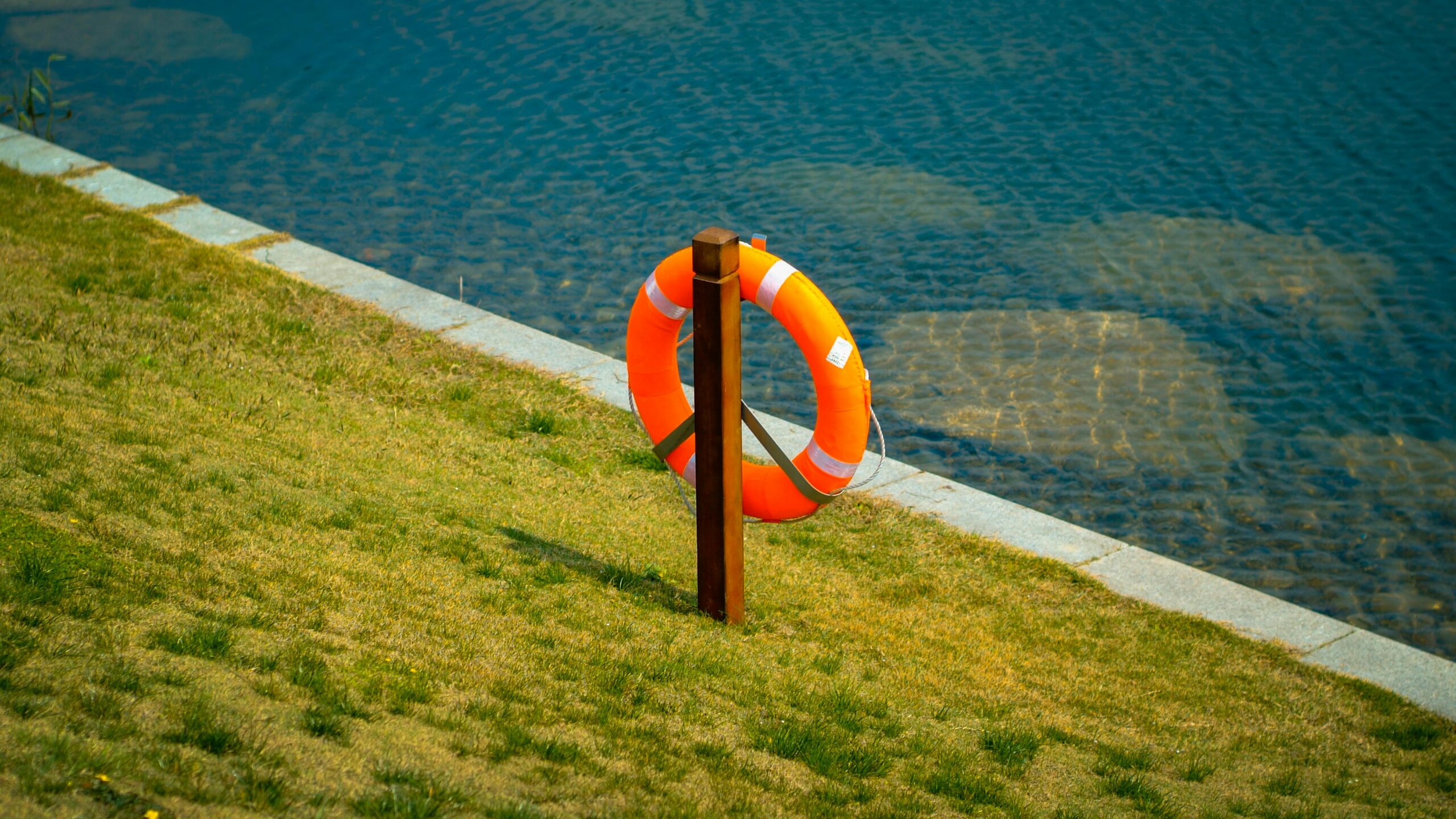 Orange lifebuoy hangs on a wooden post by a calm lake, symbolizing safety and preparedness.